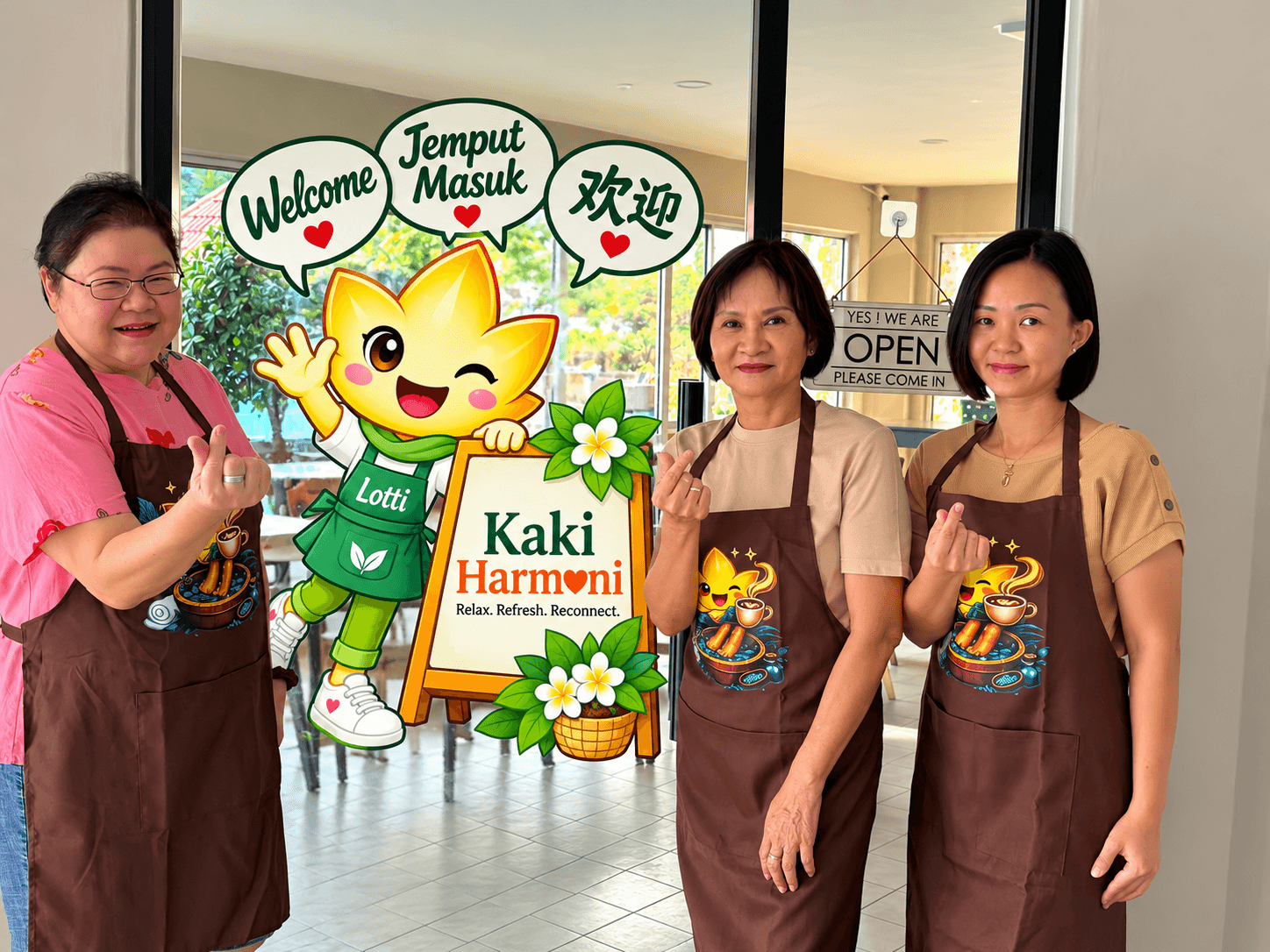 The three of us outside Kaki Harmoni in our aprons, beside Lotti's welcome sign
